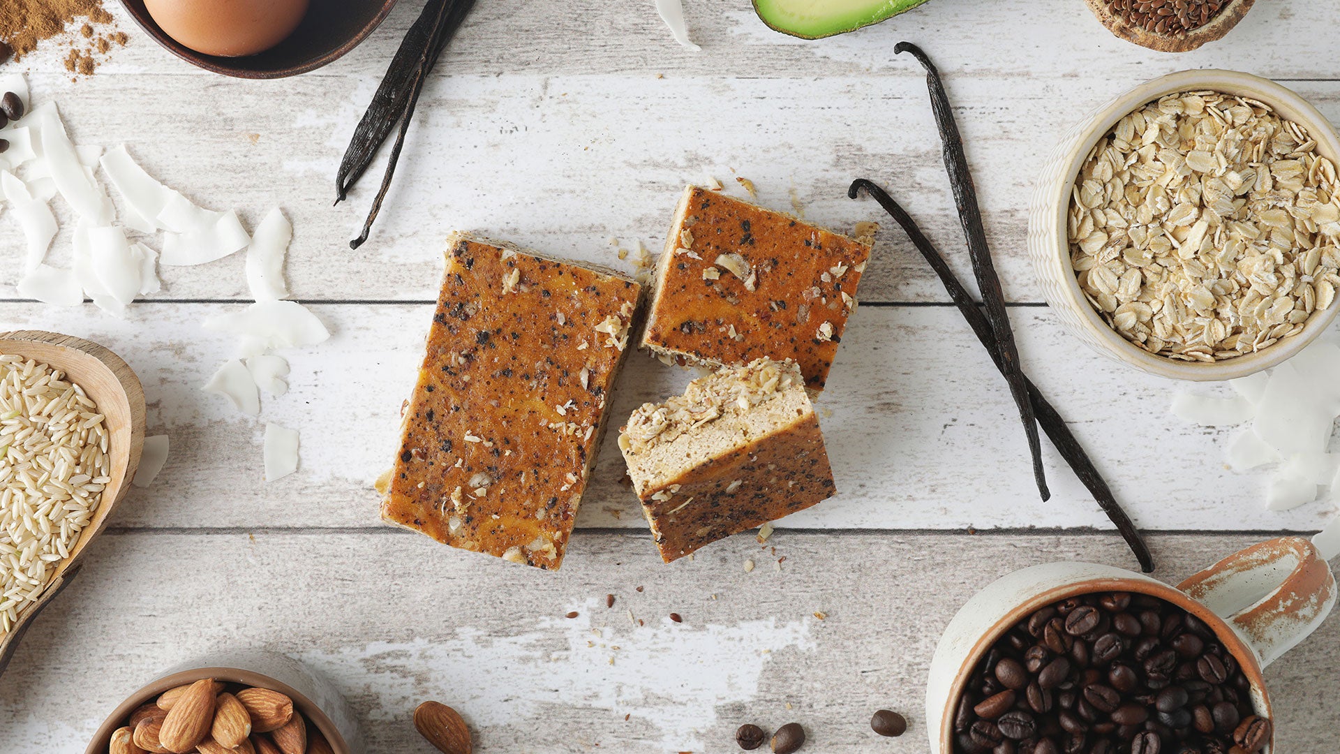 Nuts, seeds, and a C1 protein bar on a wooden surface with vanilla beans and avocados.