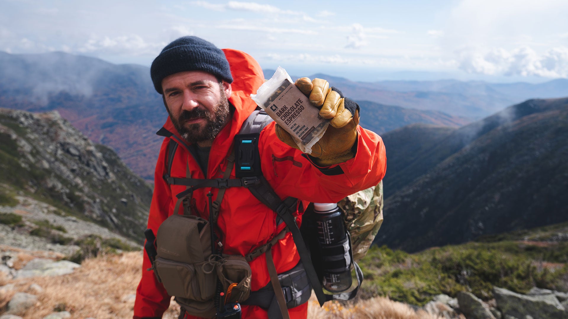 Matt DeMaio holding a Dark Chocolate Espresso Condition One Protein Bar on a mountain.