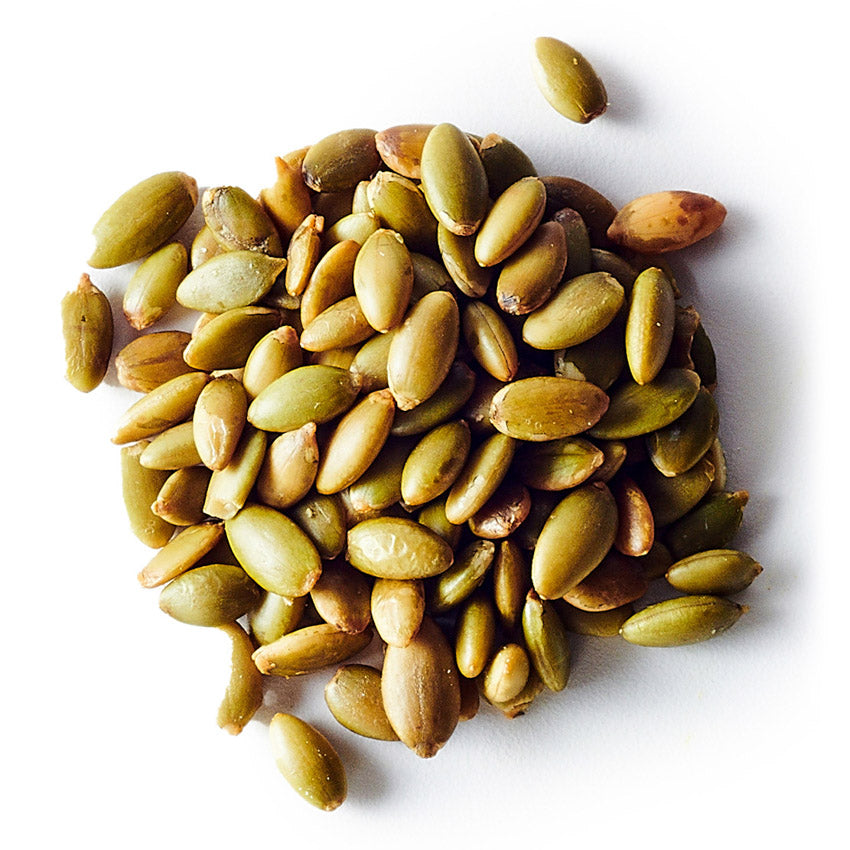 Pile of green and brown pumpkin seeds on a white background