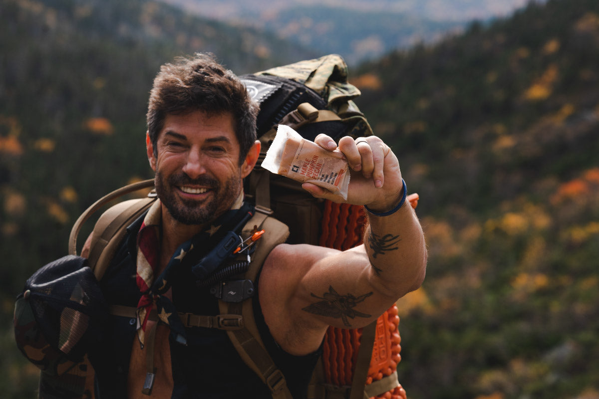 Rudy Reyes holding a Maple Pumpkin Pecan Condition One Protein bar on a hike.