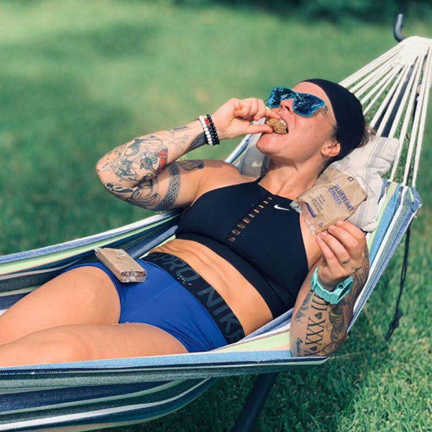 Meredith Burns lounging in a hammock outdoors, eating C1 bars and wearing sunglasses.