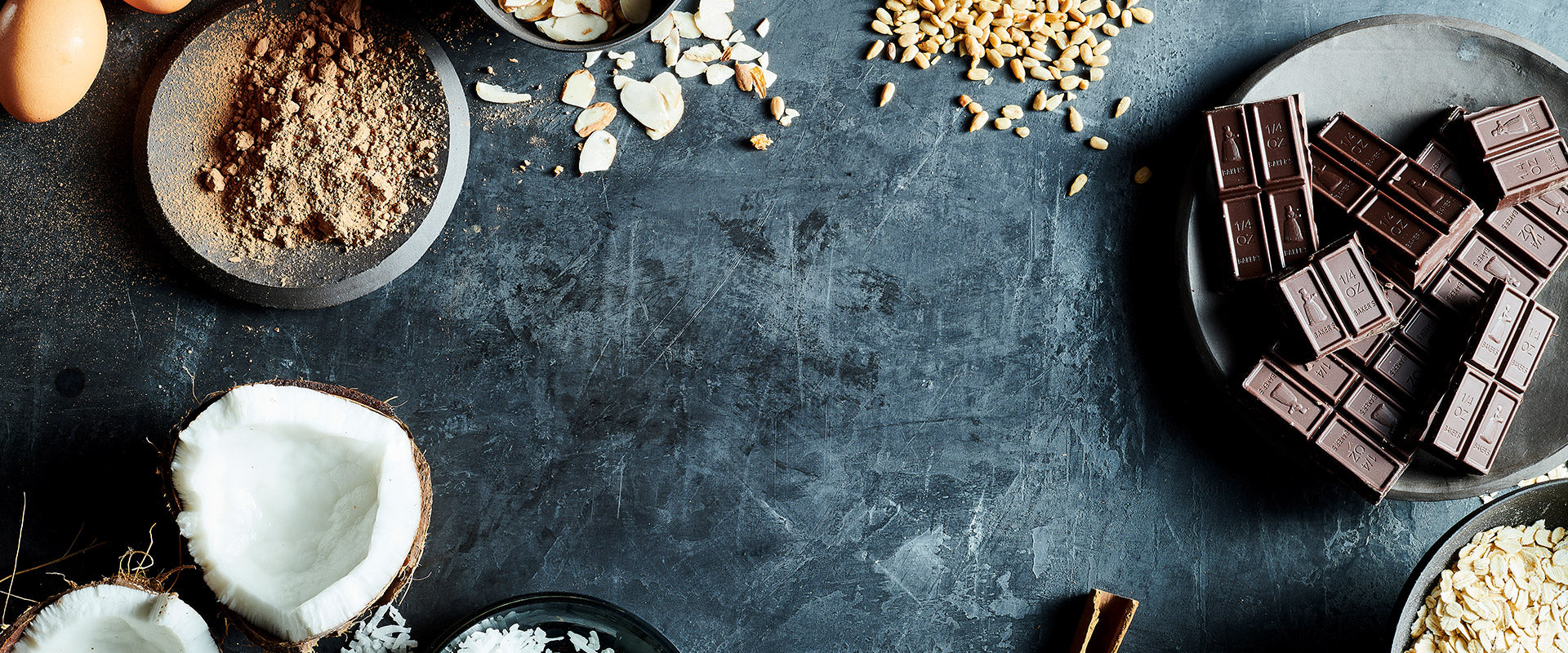 Dark chocolate bars on a dark surface with coconut, nuts, and other ingredients.