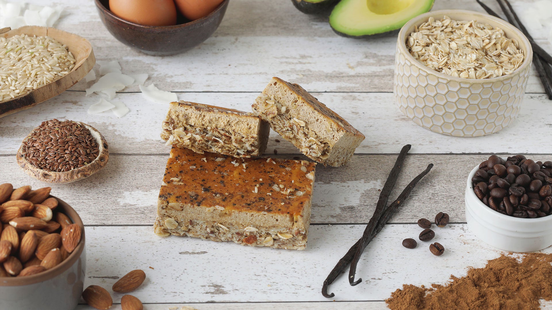 Nuts, seeds, and a C1 protein bar on a wooden surface with vanilla beans and avocados.