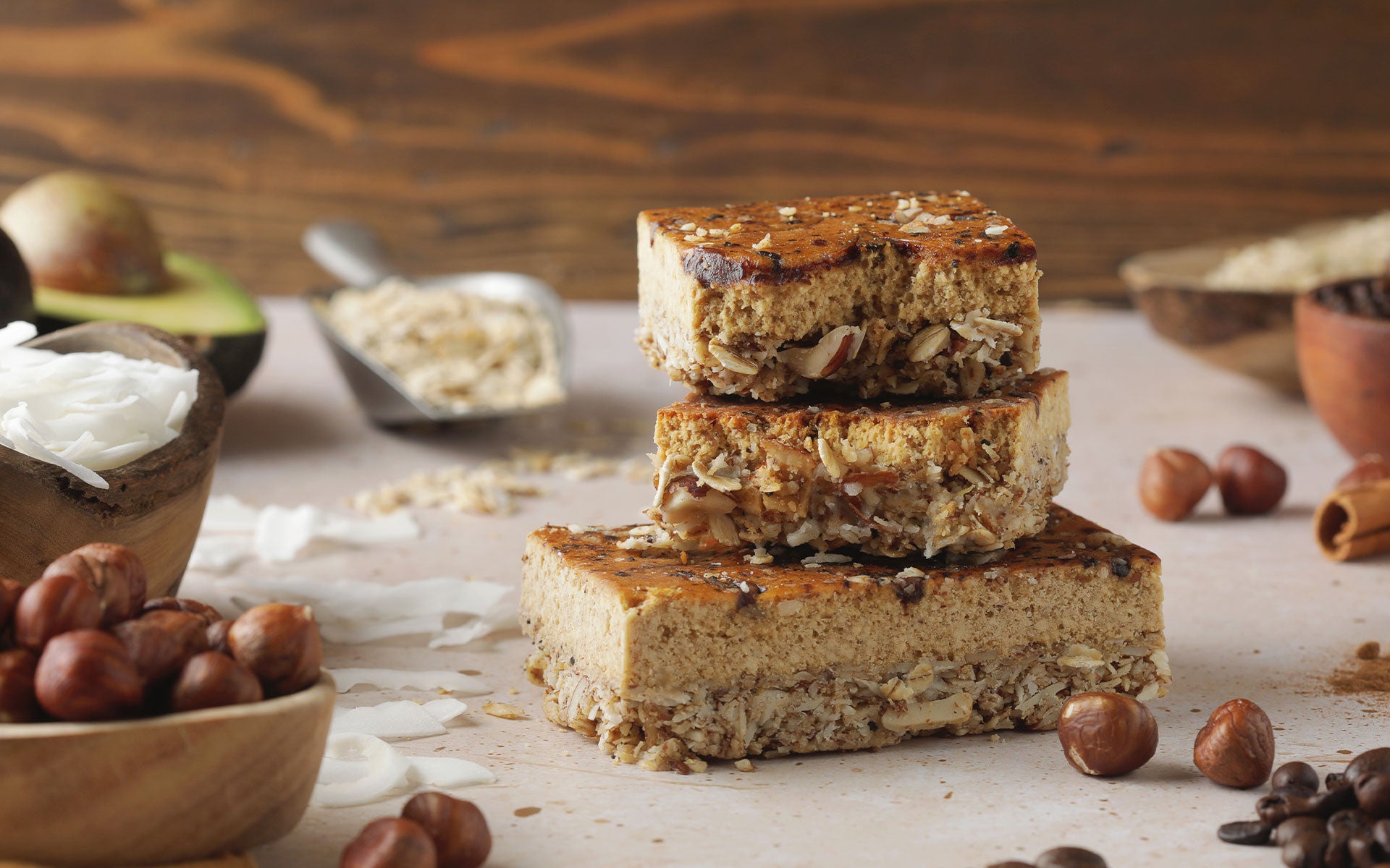 Condition One Hazelnut Macchiato Protein bar surrounded by the wholefood ingredients of the bar such as hazelnuts, coffee beans, coconut flakes, oats, cinnamon, avocado oil, and other super foods.