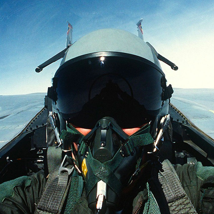 Person wearing a helmet and oxygen mask inside a cockpit with a clear sky background