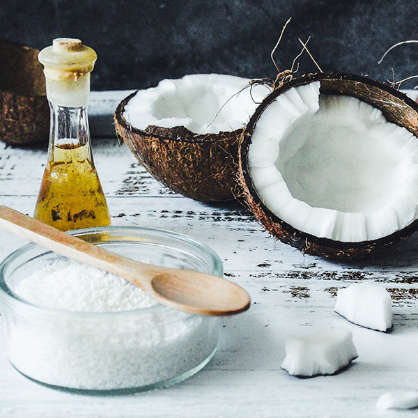 Coconut oil bottle, halved coconut, and coconut flakes on a wooden surface